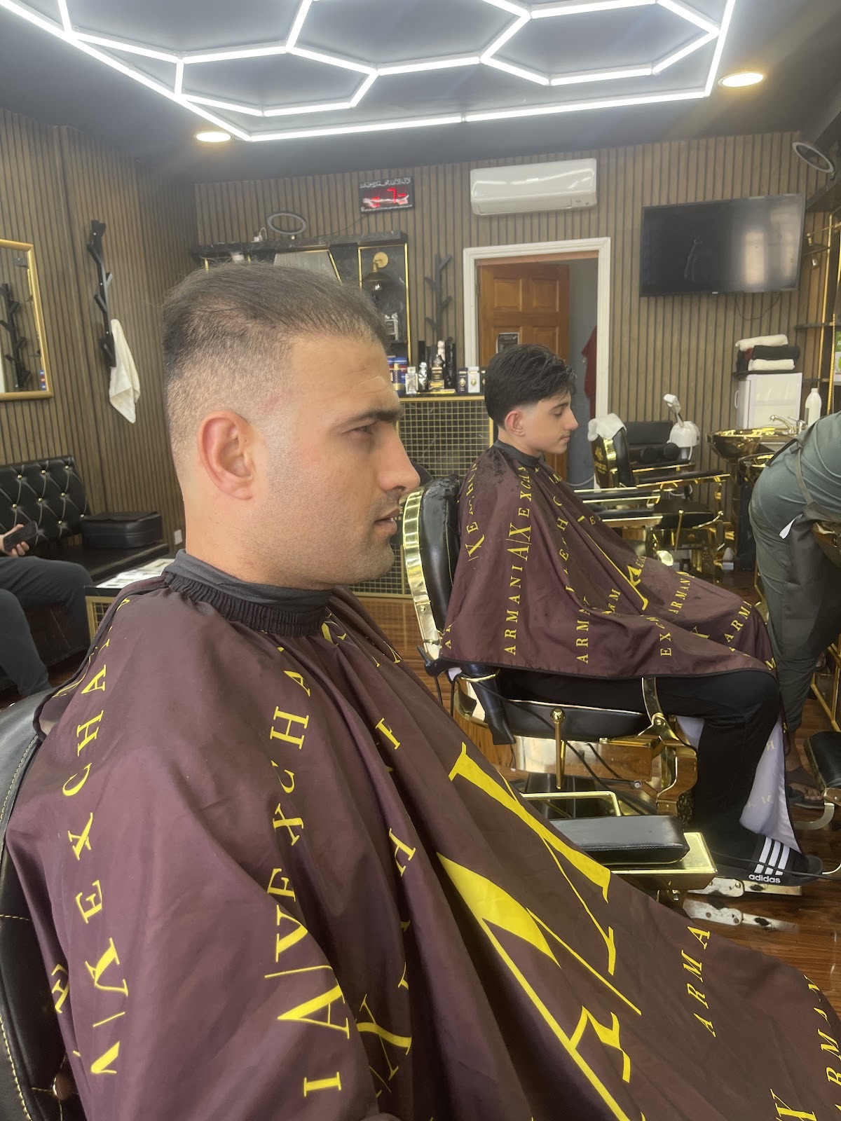 Client in a brown-and-gold cape with a fresh fade, the shop's chairs behind him